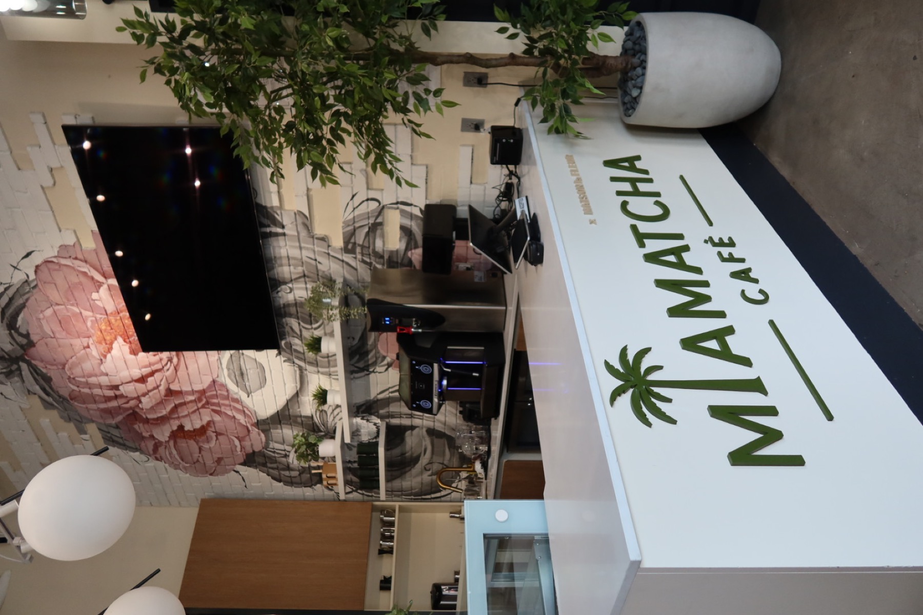 MiaMatcha Café counter with the palm-tree logo and a blush peony floral mural