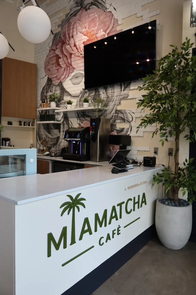 MiaMatcha Café counter with the palm-tree logo and a blush peony floral mural